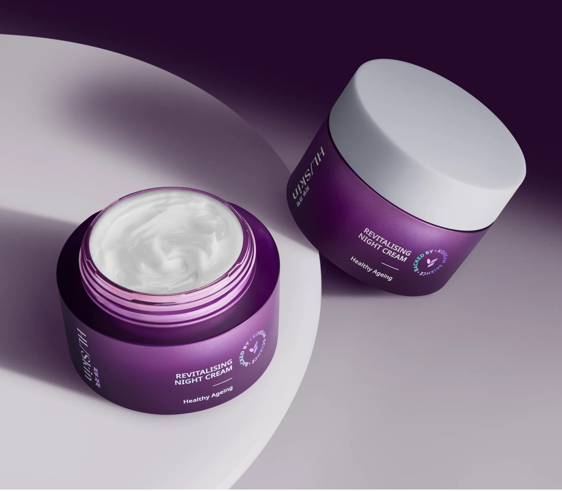 Purple skincare jar with white lid, angled on a soft gray surface; label reads 'REVITALISING NIGHT CREAM' (Healthy Ageing).